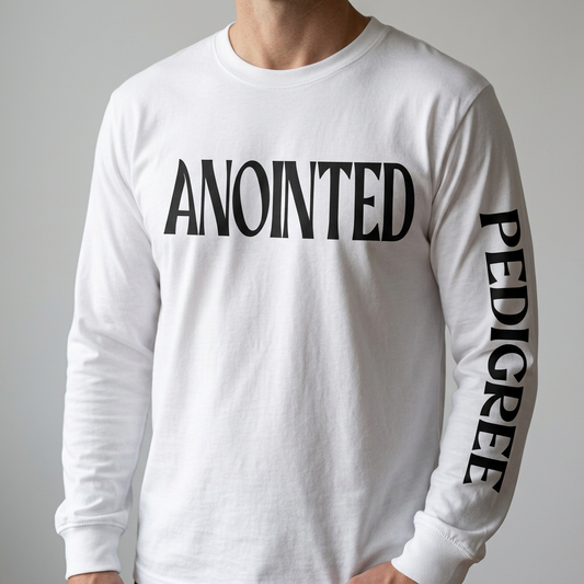 Photographic-style mockup of black ANOINTED chest lettering and PEDIGREE sleeve lettering in vinyl on a white long-sleeve tee.